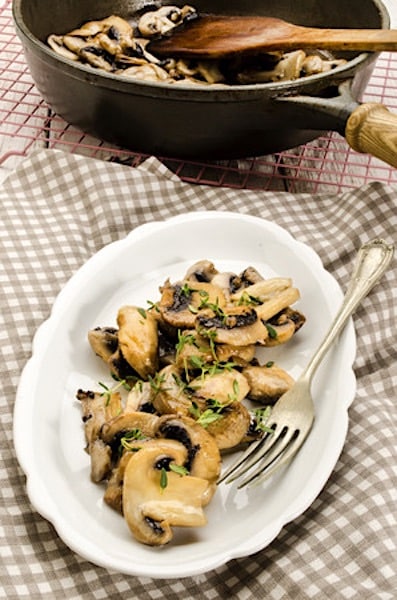 79453136 – fried mushroom slices and thyme on a plate and in a pan