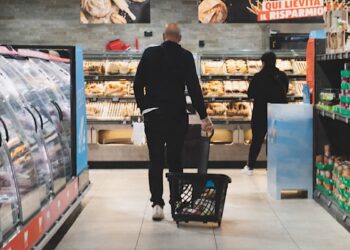 mangiare con pochi soldi Spesa in un supermercato di una grande città: carrello con pochi prodotti davanti agli scaffali alimentari