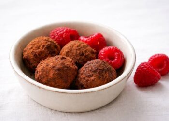 tartufi al cioccolato e lamponi spolverati di cacao in una ciotola, con lamponi freschi su tovaglia bianca